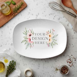 May include: White, oval-shaped serving platter with a floral design and the text "YOUR DESIGN HERE". The floral arrangement features pink and peach flowers with green leaves. Kitchen tools and ingredients surround the platter.