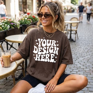 Model wearing Comfort Colors 1717 Espresso t-shirt sitting at outdoor cafe with clear front design area visible