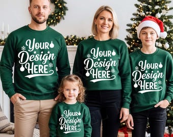 May include: A family of four wearing matching green sweatshirts with the text "Your Design Here" in white. The sweatshirts have a Christmas theme with snowflakes and ornaments. The family is standing in front of a Christmas tree and a fireplace.
