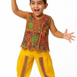 Puede incluir: Traje tradicional infantil. El conjunto incluye un sombrero amarillo, un chaleco sin mangas y un pantalón. El chaleco está adornado con bordados florales coloridos. El pantalón es amarillo con rayas bordadas. El niño sonríe y levanta el brazo.