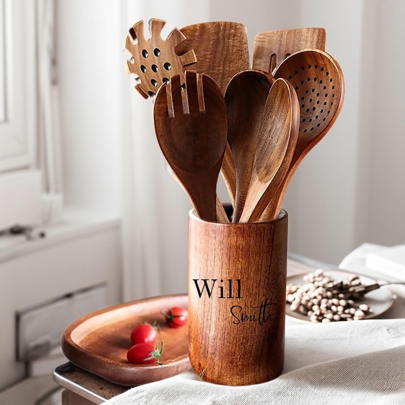 May include: A collection of wooden kitchen utensils, including spoons, spatulas, and a slotted spoon, displayed in a wooden holder. The holder is engraved with the name "Will Smith". The utensils are various shades of brown.