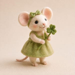 Könnte beinhalten: Eine nadelgefilzte Mausfigur mit cremefarbenem Fell, rosa getönten Ohren und rosigen Wangen. Die Maus trägt ein hellgrünes Kleid und ein passendes Stirnband mit einer kleinen Schleife und hält ein grünes vierblättriges Kleeblatt in den Pfoten.