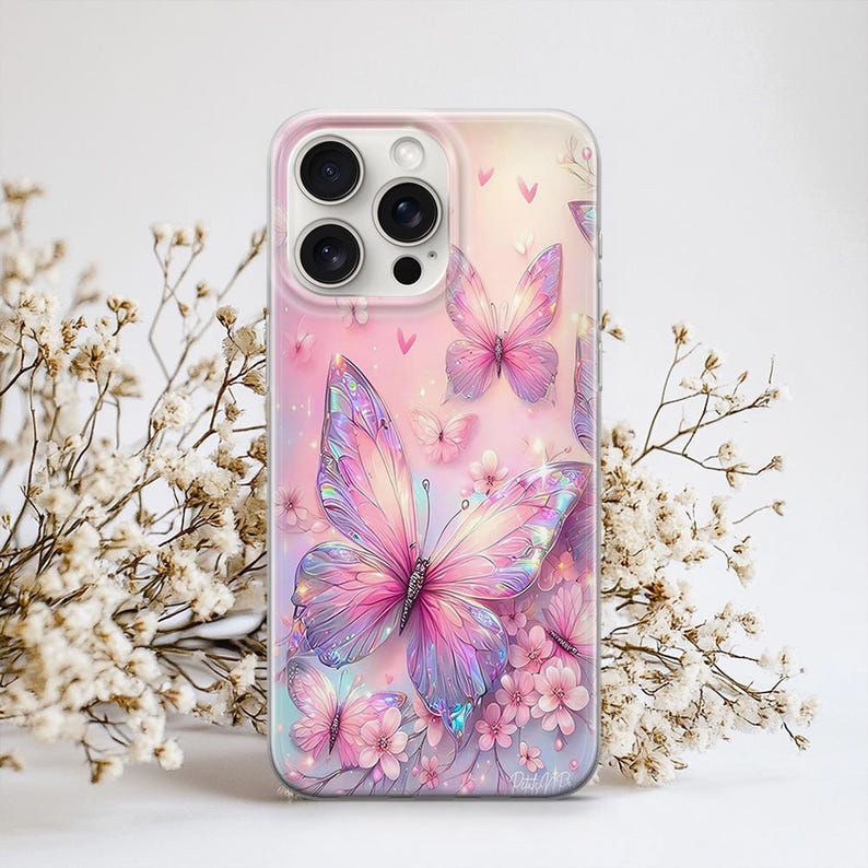 Puede incluir: Una funda de tel&eacute;fono con un dise&ntilde;o vibrante de mariposas. La funda presenta una gran mariposa iridiscente con tonos rosas, morados y azules, rodeada de mariposas m&aacute;s peque&ntilde;as y flores rosas sobre un fondo rosa suave. La funda tiene un acabado transparente y brillante.