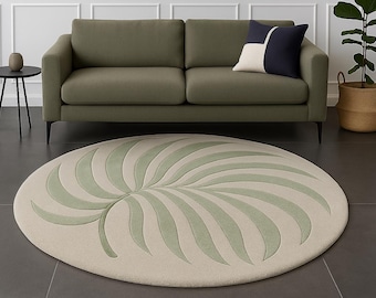 May include: A round rug with a light beige background and a large, stylized green leaf design. The rug is placed on a dark gray floor in front of a green sofa. A black side table and a woven basket with a plant are also visible.