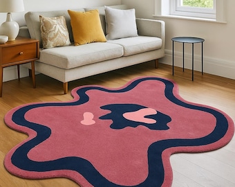 May include: A unique, abstract-shaped rug in shades of pink, navy blue, and coral. The rug features a wavy, organic design with a dark blue border and interior shapes. It's placed on a hardwood floor, complementing the room's neutral color scheme.