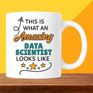May include: White ceramic mug with the text "THIS IS WHAT AN Amazing DATA SCIENTIST LOOKS LIKE" in black, orange, and teal. The mug has a curved handle and is set against a yellow and orange background.