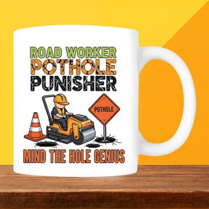 May include: White ceramic mug with a road worker design. The mug displays the text "ROAD WORKER POTHOLE PUNISHER MIND THE HOLE GENIUS" in green, orange, and black. A cartoon road worker operates a roller, with a traffic cone and a pothole sign.