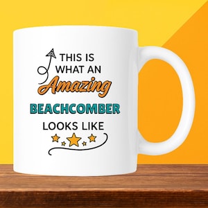 May include: White ceramic mug with the text "THIS IS WHAT AN Amazing BEACHCOMBER LOOKS LIKE" in black, orange, and teal. The mug has a curved handle and is set against a yellow and orange background.