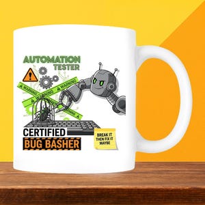May include: White ceramic mug with a robot design and the text "AUTOMATION TESTER" and "CERTIFIED BUG BASHER". The design includes a bug in a cage and a keyboard, with the phrase "BREAK IT THEN FIX IT MAYBE".
