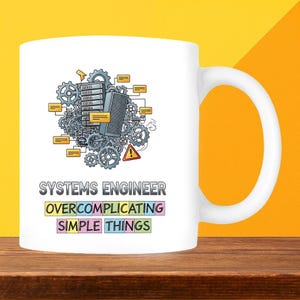 May include: White ceramic mug with a handle, featuring the text "SYSTEMS ENGINEER OVERCOMPLICATING SIMPLE THINGS." The mug has a graphic of gears, servers, and warning signs.