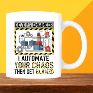 May include: White ceramic mug with a black and yellow graphic. The graphic reads "DEVOPS ENGINEER" above an illustration of machinery and "I AUTOMATE YOUR CHAOS THEN GET BLAMED" below. The mug has a white handle and is on a wooden surface.