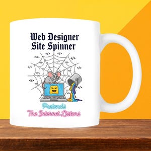 May include: White ceramic mug with the text "Web Designer Site Spinner" and a cartoon illustration. The illustration features a mouse, a laptop, a spider web, and a bucket pouring colourful liquid. The text "Pretends The Internet Listens" is also included.