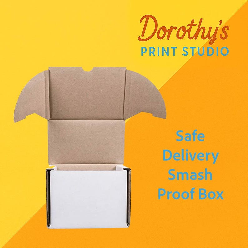 Op de afbeelding: Een open kartonnen doos met een witte binnenkant, tegen een gele en oranje achtergrond. De tekst "Dorothy's PRINT STUDIO" staat in de rechterbovenhoek, met "Safe Delivery Smash Proof Box" in blauwe tekst.