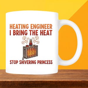 May include: White ceramic mug featuring the text "HEATING ENGINEER I BRING THE HEAT" in orange and red. The mug has an illustration of a radiator with flames and the words "STOP SHIVERING PRINCESS".