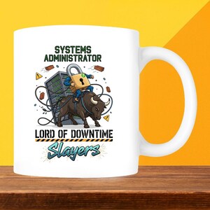 May include: White ceramic mug with a humorous graphic. The design features a cartoon of a person riding a bull, with a server rack and lock, and the words "SYSTEMS ADMINISTRATOR" and "LORD OF DOWNTIME Slayers".