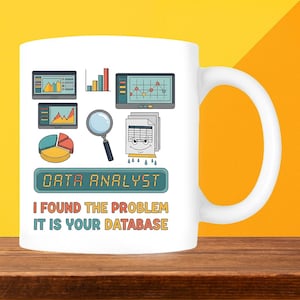 May include: White ceramic mug with a large handle, featuring a colourful design for a data analyst. The design includes charts, graphs, a magnifying glass, and the text "DATA ANALYST I FOUND THE PROBLEM IT IS YOUR DATABASE."