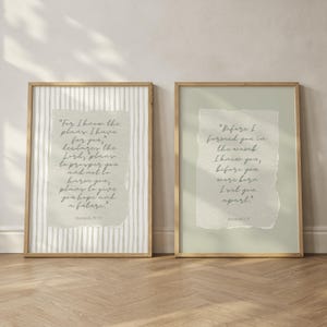 Op de afbeelding: Twee ingelijste kunstdrukken met goudkleurige frames. De prints bevatten tekst op getextureerde, lichtgekleurde achtergronden. Eén print heeft een gestreepte achtergrond, de andere een effen achtergrond. De tekst is handgeschreven.