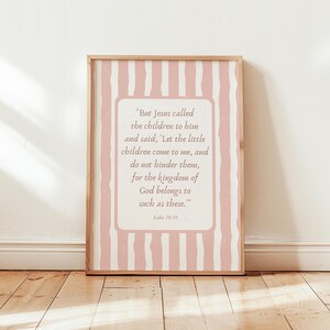 Op de afbeelding: Een ingelijste print met een licht houten frame. De print heeft een roze en witte gestreepte achtergrond met een centraal crèmekleurig rechthoek met een citaat uit Lucas 18:16.