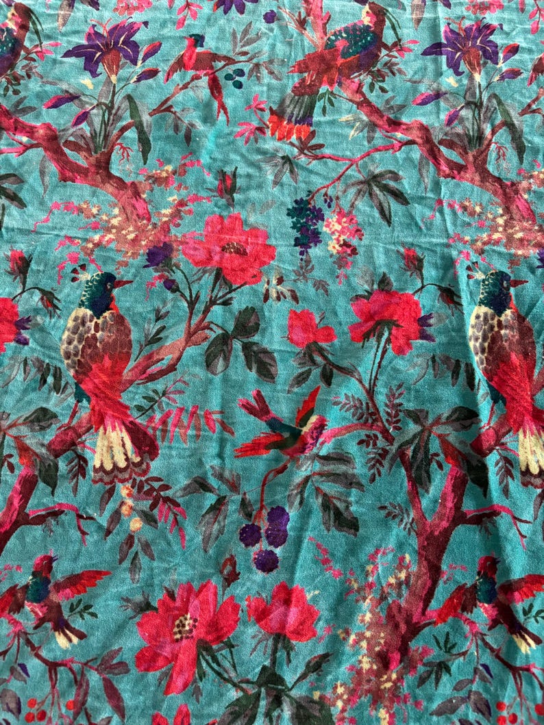 May include: A teal fabric featuring a repeating pattern of birds with red, yellow, and dark blue plumage perched on dark red branches. The design includes large pink and red flowers, dark purple berries, and green leaves throughout the textile.