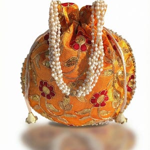 Könnte beinhalten: Eine orangefarbene, runde Beuteltasche mit Kordelzug und Perlenhenkel. Die Tasche ist mit goldenen und roten Blumenmustern und goldenen Pailletten bestickt. Die Kordel endet in goldenen Quasten.