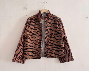May include: A long-sleeve jacket featuring a brown and black tiger stripe pattern on the exterior. The garment has a high collar, a front zipper closure, and a visible interior lining with a vertical black and white pinstripe design.