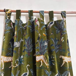 May include: Olive green velvet curtains with a jungle-themed pattern. The design features leopards, zebras, birds, and tropical plants. The curtains are hung with green fabric loops on a copper rod.
