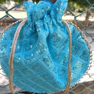 Può includere: Una borsa turchese con coulisse e motivo a rombi, impreziosita da paillettes e perline color oro. La borsa ha una chiusura con coulisse con nappe color oro e un manico con perline. La borsa è realizzata in un tessuto morbido e strutturato.
