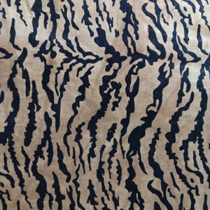 Könnte beinhalten: Nahaufnahme eines Stoffes mit Tigerstreifenmuster. Der Hintergrund ist hellbraun und die Streifen sind schwarz. Der Stoff hat eine weiche, samtige Textur.