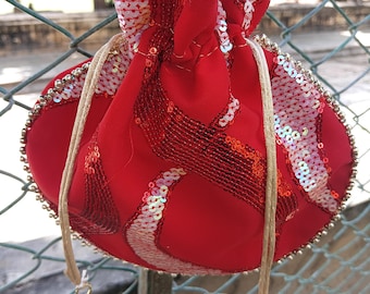 May include: A red drawstring pouch with a sequined design. The pouch has a gold beaded trim and a drawstring closure. The drawstring is made of a beige rope and has pearl and gold bead accents.