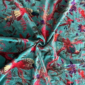May include: A teal velvet fabric featuring a repeating pattern of birds perched on branches with red and pink flowers. The birds have red, yellow, and dark green plumage. The fabric has a soft, plush texture with a visible sheen across the surface.