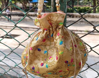 May include: A gold-colored drawstring bag with intricate embroidery and colorful floral patterns. The bag features a beaded strap and decorative tassels. The bag is hanging on a green metal pole.