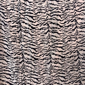 May include: A fabric featuring a repeating black tiger stripe pattern printed on a light beige background. The material has a visible crinkled texture throughout, creating a series of horizontal folds and creases across the entire surface.