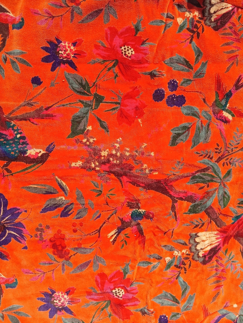 May include: Bright orange fabric with a floral and bird design. The pattern includes red and pink flowers, blue and purple details, and colourful birds on branches. Green leaves and berries complete the botanical theme.