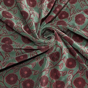 May include: Green fabric with a floral pattern in burgundy. The fabric is soft and has a velvet texture. The floral design features large, stylized flowers and winding vines.