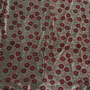 May include: Close-up of a fabric with a repeating floral pattern. The flowers are a deep burgundy color, and the background is a muted green. The flowers are arranged in a symmetrical design with curved stems and leaves.