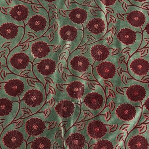 May include: A repeating pattern of burgundy flowers and vines on a muted green background. The floral design features large, round blooms with detailed centers and delicate leaves, creating a vintage aesthetic. The fabric has a soft, textured appearance.