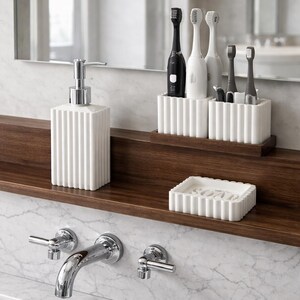 May include: A modern bathroom setup featuring a white soap dispenser, toothbrush holders, and a soap dish. The items are arranged on a dark wooden shelf against a marble wall. The design is minimalist and clean.