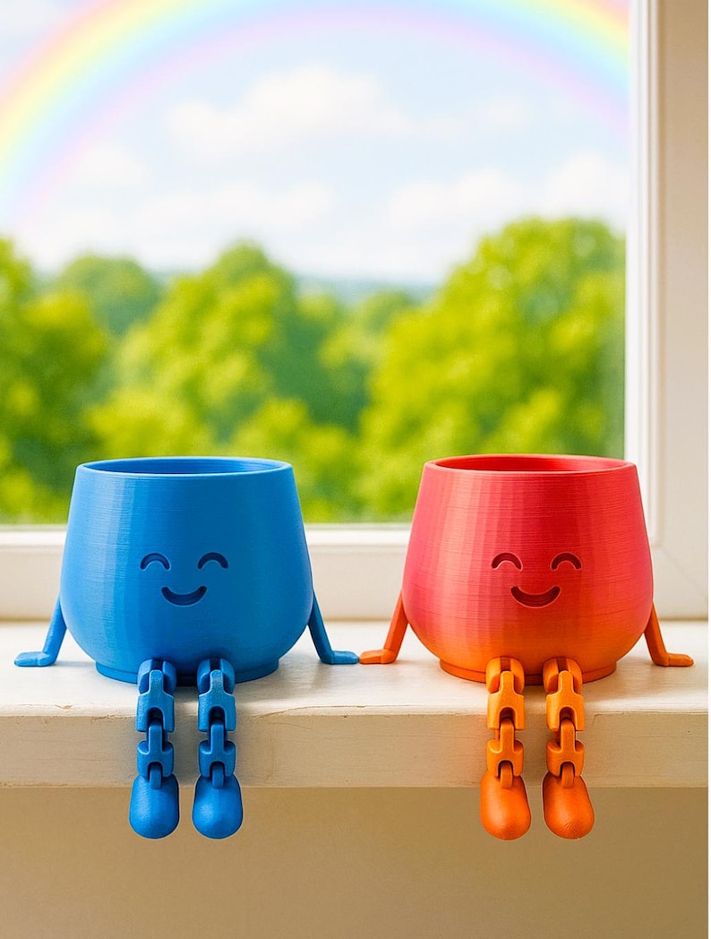 May include: Two smiling, anthropomorphic planters sit side-by-side on a windowsill. One is blue, the other is red-orange. Both have arms and segmented legs, and a rainbow is visible in the background. These planters are a fun and whimsical addition to any home.