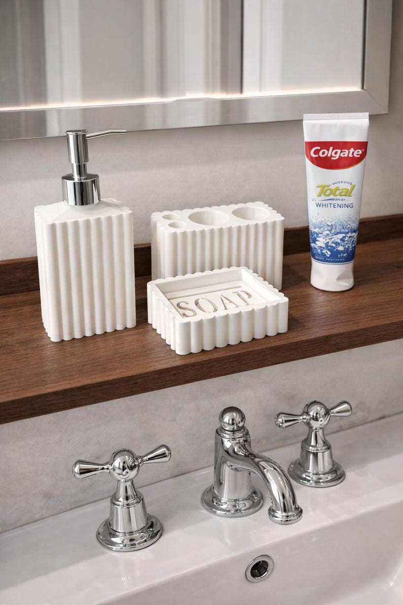 May include: A white bathroom set with a ribbed design, including a soap dispenser, toothbrush holder, and soap dish. A tube of Colgate Total Whitening toothpaste is also present. The set is on a wooden shelf above a chrome faucet.