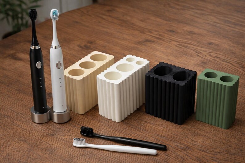 May include: A collection of modern bathroom accessories, including two electric toothbrushes, toothbrush holders, and manual toothbrushes. The holders come in beige, white, black, and green. The toothbrushes are black and white.