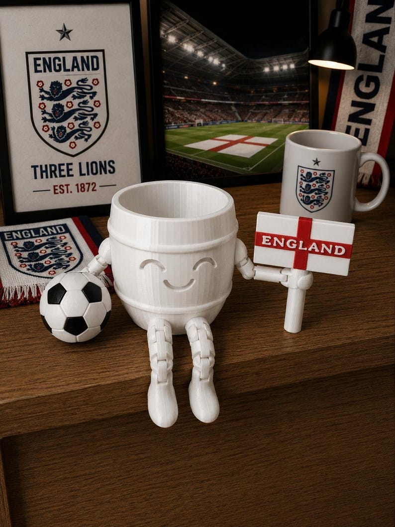 May include: A white, smiling barrel-shaped figurine with articulated legs and arms, holding a sign that reads "ENGLAND." A soccer ball and a mug with the England emblem are also present, along with framed artwork and a scarf.