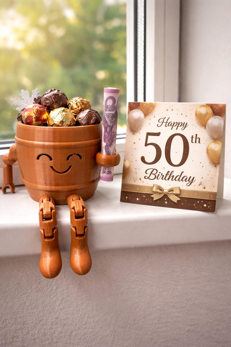 May include: A whimsical brown barrel-shaped container with a smiling face, holding wrapped chocolates and a rolled-up bill. A birthday card with "Happy 50th Birthday" is next to it. The barrel has legs and arms.