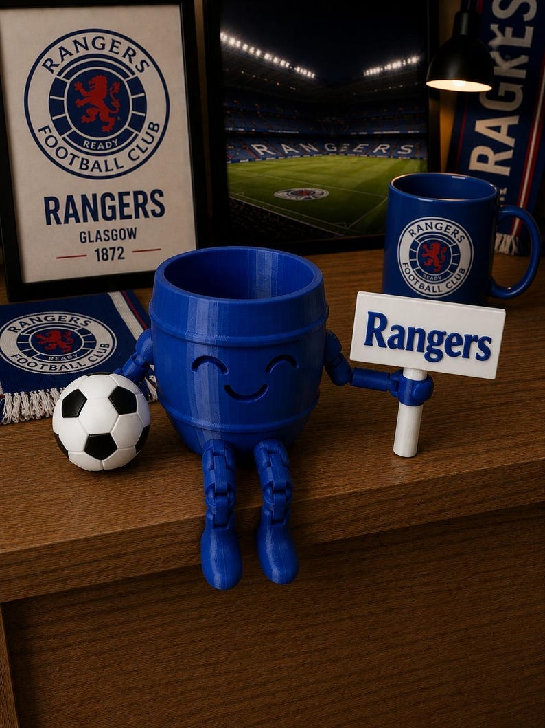 May include: A blue 3D-printed barrel-shaped figure with a smiling face, holding a sign that reads "Rangers." A soccer ball and a mug with the Rangers logo are also visible. The image includes framed artwork and a scarf with the Rangers logo.