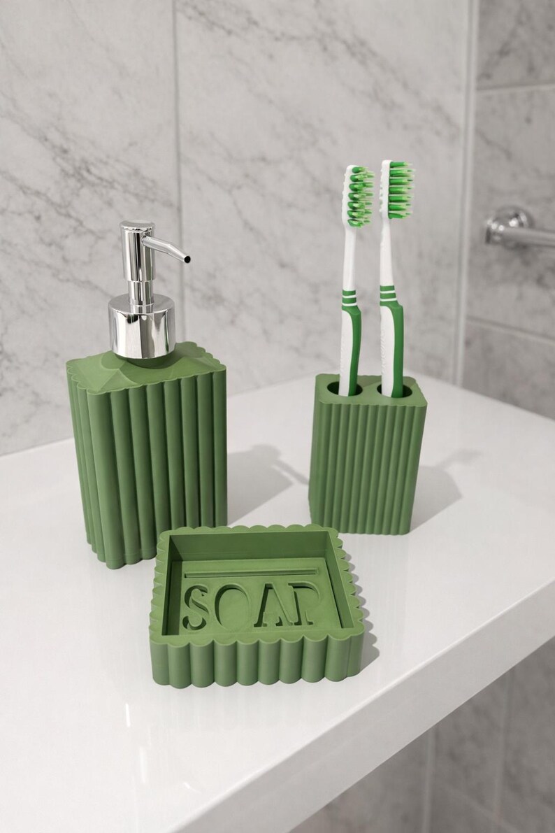 May include: A green bathroom set includes a soap dispenser with a silver pump, a toothbrush holder with two toothbrushes, and a soap dish with the word "SOAP". The set has a ribbed design.