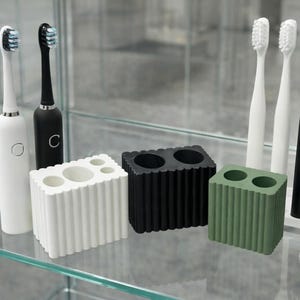 May include: A collection of dental hygiene products, including electric toothbrushes and toothbrush holders. The toothbrushes are white and black, with blue and black bristles. The holders are white, black, and green, with a ribbed design.