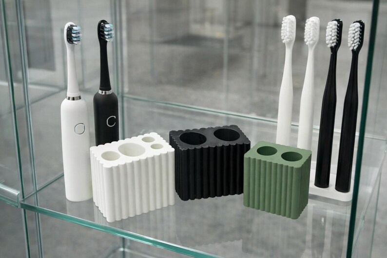 May include: A collection of dental hygiene products, including electric toothbrushes and toothbrush holders. The toothbrushes are white and black, with blue and black bristles. The holders are white, black, and green, with a ribbed design.