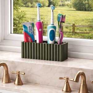 Puede incluir: Un soporte para cepillos de dientes verde oscuro con un dise&ntilde;o acanalado contiene dos cepillos de dientes el&eacute;ctricos, un cepillo de dientes manual y un tubo de pasta de dientes. Los cepillos de dientes son rosas, azules y verdes. El tubo de pasta de dientes tiene detalles azules y rojos.