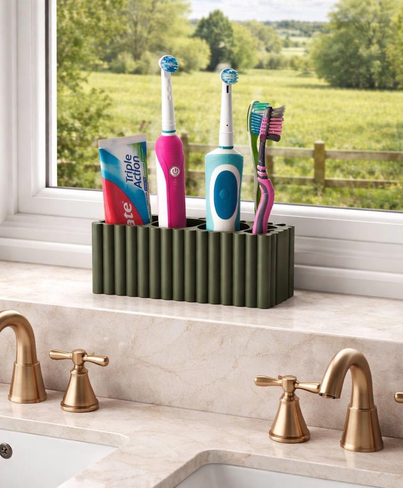 Puede incluir: Un soporte para cepillos de dientes verde oscuro con un dise&ntilde;o acanalado contiene dos cepillos de dientes el&eacute;ctricos, un cepillo de dientes manual y un tubo de pasta de dientes. Los cepillos de dientes son rosas, azules y verdes. El tubo de pasta de dientes tiene detalles azules y rojos.