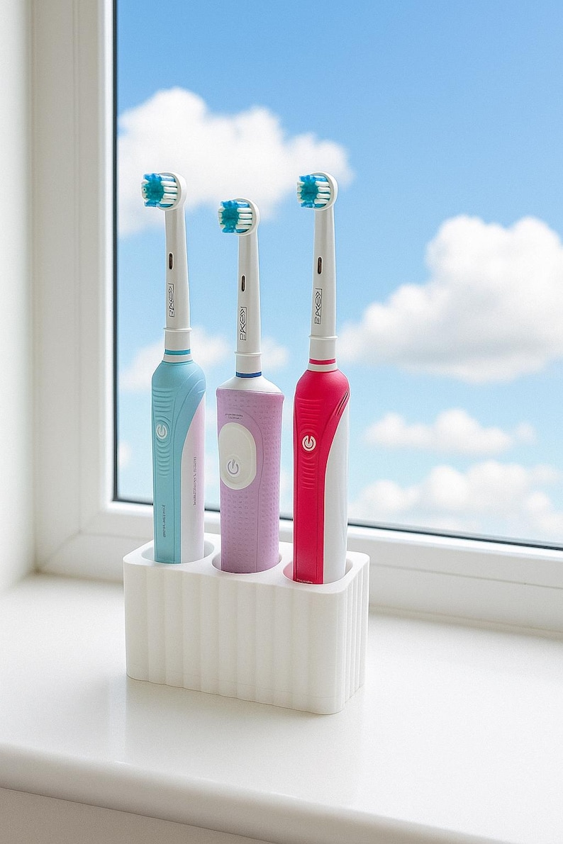 Puede incluir: Tres cepillos de dientes el&eacute;ctricos en un soporte blanco. Los cepillos de dientes son de color azul claro, lavanda y rojo, con cabezales blancos y azules. El soporte est&aacute; sobre un alf&eacute;izar blanco con cielo azul y nubes al fondo.