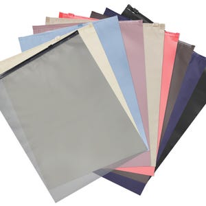May include: A collection of colorful, rectangular zipper pouches in various shades, including gray, pink, blue, and black. Each pouch has a black zipper closure and is arranged in a fan shape.